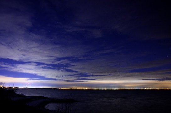 The western tip of Lake Ontario glows at night with light pollution. A few stars try hard to peek through the clouds.